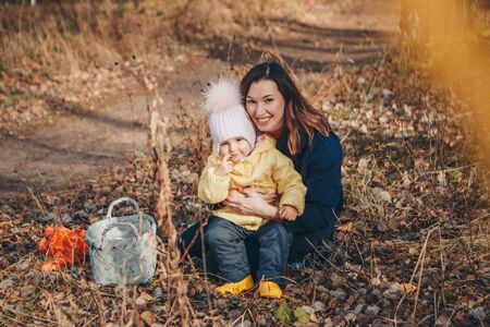 a small child with his mother in a warm suit walking in woods. The woman and girl collect leaves in...
