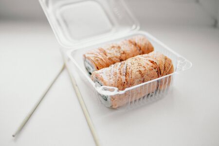 Japanese cuisine: rolls in a plastic container. Sushi on white background. Advertising concept of traditional Oriental cuisine, fish food: salmon, tuna, riceの写真素材