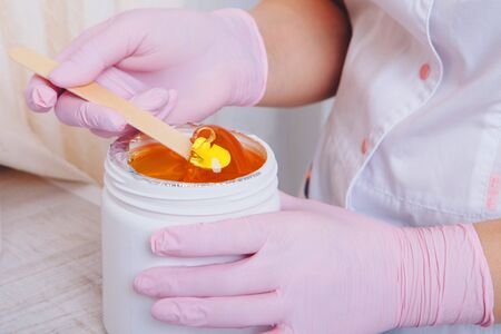 Wax for depilation close-up. girl pulls out cosmetic product from jar. Hand with wooden stick for cosmetic procedures. Sugaring: epilation with liquate sugar at legsの写真素材
