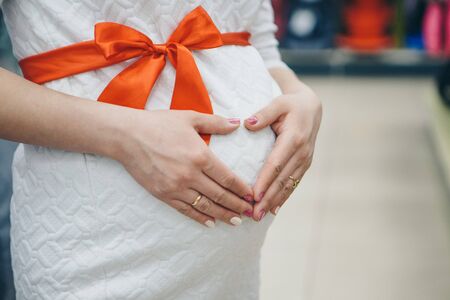 Heart symbol folded from the hands. a pregnant woman is stroking her stomach. Copy space. Healthy lifestyle concept, IVF, mother's day, international women's day, Valentine's dayの写真素材
