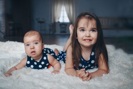 the concept of a healthy lifestyle, the protection of children, shopping - a teenager with a newborn baby playing together. Happy kids: sisters lying on the floor on white background.の写真素材