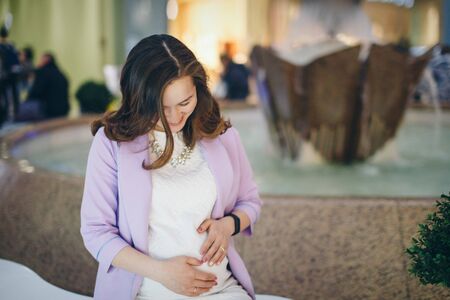 a pregnant woman is stroking her stomach. a girl waiting for a child walks in a shopping center. The concept of a healthy lifestyle , IVF, fashion for pregnant women, childrenの写真素材