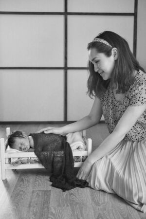 a mother strokes a baby who is lying in a wooden bed under a blanket. portrait of a small child. concept of childhood, health, IVF, children's furniture, interior, wood productsの写真素材