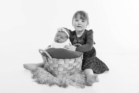 the concept of a healthy lifestyle, child protection, IVF-teen with a newborn baby on the floor. Baby in the basket. Happy children: sisters on a white backgroundの写真素材