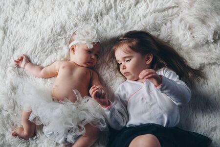 the concept of a healthy lifestyle, the protection of children, shopping - a teenager with a newborn baby playing together. Happy kids: sisters lying on the floor on white background. the view from the topの写真素材