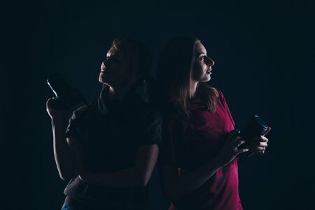 two girls with cameras back to back. photographers on a dark background.