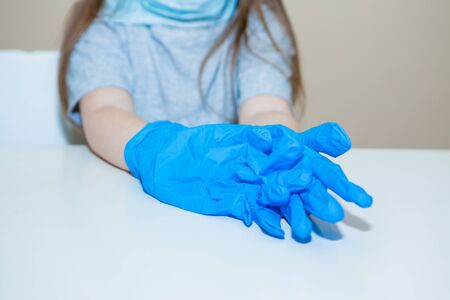The doctor pulls on a pair of rubber gloves. the medic is preparing for surgery. a little girl in a mask plays in the hospitalの写真素材