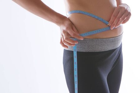 the result of sports exercises: a toned stomach close-up on a white background. The girl measures her waist with a centimeter tape. Influence of dietの写真素材