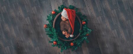 a newborn baby sleeps in a red cap with a pompom in a Christmas wreathの写真素材