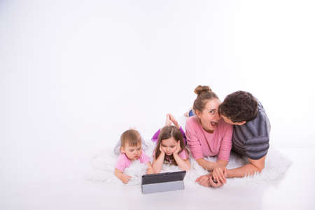the kids are watching cartoons on the tablet. a man and a woman embrace. Family vacation, joint pastime. Parents with girls on the floorの写真素材