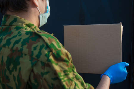 the military delivers food to your home. assistance to pensioners, the poor and the population. a courier in rubber gloves holds a box on a black background.の写真素材