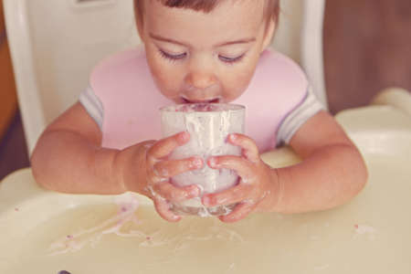 portrait of a child who drinks yogurt from a glass. smeared face with foodの写真素材