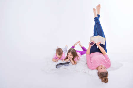 a woman with phone reads a book, children watch a cartoon on a tablet. Hobbies and recreation with...