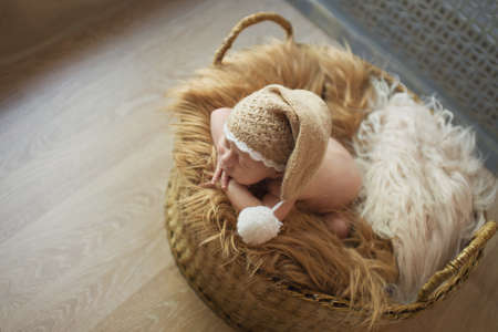 a small child in a basket sleeps in a warm knitted hat with a pompomの写真素材
