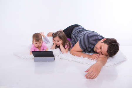 the kids are watching cartoons on the tablet. a man sleeps. Family vacation, joint pastime. Parents with girls on the floorの写真素材