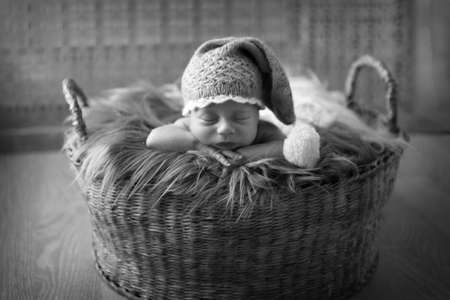 a small child in a basket sleeps in a warm knitted hat with a pompom