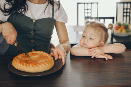 the family eats cakes. dinner at the bakery. feast in the kitchen. the butchering of the food. a woman cuts a pie with a knifeの写真素材