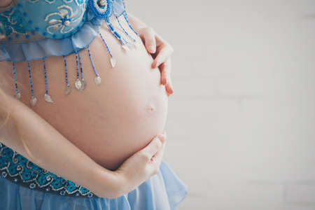 Isolated photo on a white background: a beautiful pregnant woman in a blue dress put her hands on her stomachの写真素材