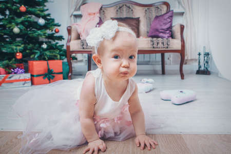 a small child meets Christmas in a crib next to a Christmas tree. New year's interior in the house.の写真素材