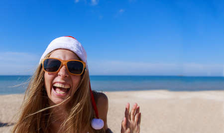 new year's eve on the beach by the sea. a girl in a Christmas hat is sunbathing in the sun. woman in sunglasses. blue sky like a copy spaceの写真素材
