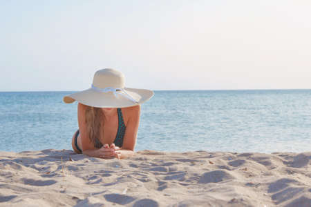 journey to the sea. girl in a bathing suit and hat sunbathing on the beach. tourist sitting on the sand. leisure wear. copy spaceの写真素材