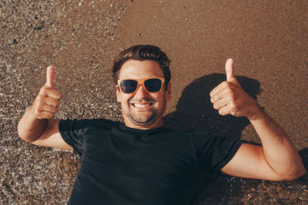 a contented man in sunglasses with his hands behind his head by the water. vacation by the sea. Refreshing treatmentsの写真素材