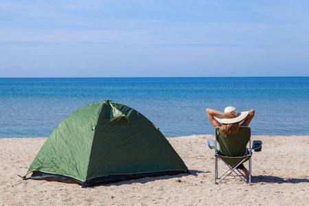 journey to the sea. camping on the beach. Vacation by the water. Men and a tent with a tourist chair on the sandの写真素材