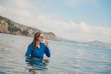 a happy girl sits in the river and drinks water from a glass. Concept of clean natural sources, environmental protectionの写真素材