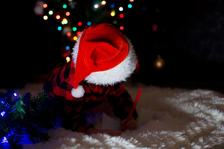 a child in red clothes is sitting waiting for the new year. the concept of celebrating Christmas at midnight. holiday costume. a girl writes a letter to Santa Claus. wish listの写真素材