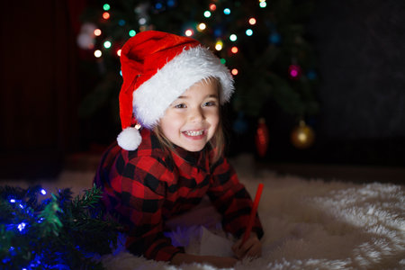 a child in red clothes is sitting waiting for the new year. the concept of celebrating Christmas at midnight. holiday costume. a girl writes a letter to Santa Claus. wish listの写真素材
