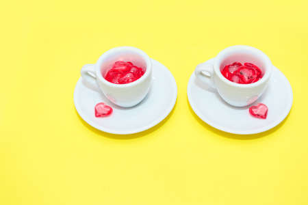 two cups with hearts on a red background. the view from the top. red hearts spilled out. isolated on a yellowbackground. copy space. pantonの写真素材