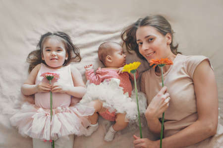 portrait of three girls with flowers. a sleeping newborn baby, a little girl and a woman lie on the floor. flowers as interior decorations. March 8の写真素材