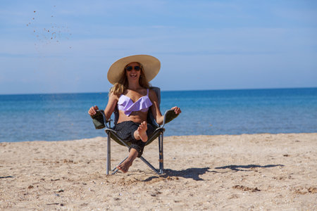 journey to the sea. girl in a bathing suit and hat sunbathing on the beach. tourist sitting on the sand. leisure wear. copy spaceの写真素材