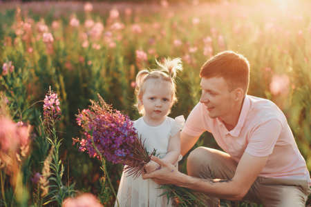 a happy father with daughter walks through a flower meadow. Love and spring blooming. Man and little girl. Father's dayの写真素材