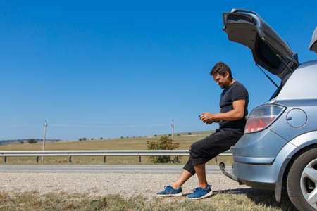 the guy looks for the road in the navigator on the phone. the tourist stopped on the road. man and open car trunk. travel by carの写真素材