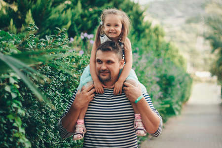 a small child sits on the father's neck. daddy's daughter is on vacation. tropical leaves. Travel to hot countriesの写真素材