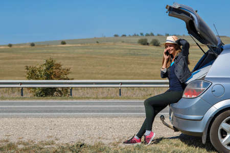 a woman makes a phone call. the tourist stopped on the road. travel by car. calling for car repairsの写真素材