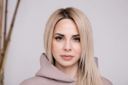 Winter came but not in heart. Portrait of warm and tender sweet blond girl with blue eyes in hoodie giggling and making flirty gazes at camera smiling delighted having good mood over white backgroundの写真素材