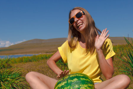 a girl sits on the beach and holds a watermelon. ripening of summer berries Joyful emotions and mood. Summer picnic.の写真素材