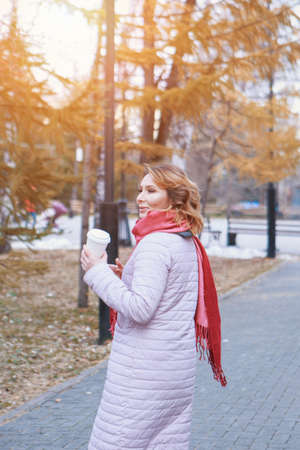 lunch break. A girl eats a pie and drinks coffee in the park on a bench. Food delivery. The desire to warm up on an autumn dayの写真素材