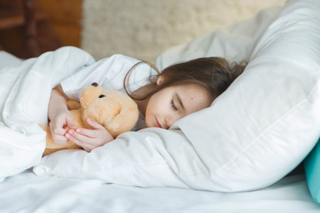 baby lying in bed with Taddy Bear. Little girl sleeps with knitted toyの写真素材