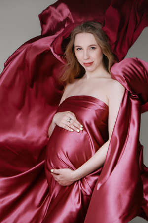 Pregnant girl in red dress. beautiful fabric texture on a light backgroundの写真素材