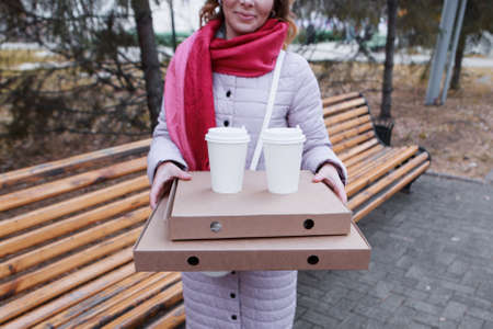 lunch break. A girl eats a pie and drinks coffee in the park on a bench. Food delivery. The desire...