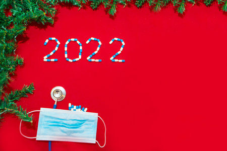 ncov-19 and the New year. Holiday in self-isolation, hospital. Christmas decorations and medical devices syringe and santa hat. Copy space on a red backgroundの写真素材