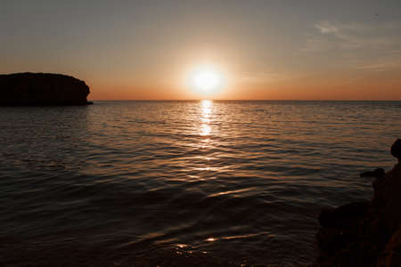 waves wash the rocky shore of the sea. Sunset. Reflection in the water of the bridge and raysの写真素材