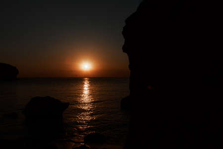 waves wash the rocky shore of the sea. Sunset. Reflection in the water of the bridge and raysの写真素材