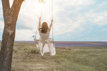 girl on a swing wrapped in green foliage. They are dressed in white robes. The sun shines on themの写真素材