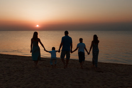 big family on the beach. Silhouettes of people against the sunset. 5 people holding handsの写真素材