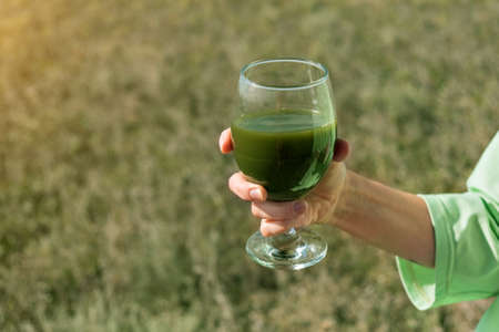 Wheat germ juice, matcha tea. Healthy food in hand. A woman drinks in the fresh airの写真素材