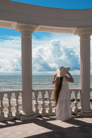 woman with long hair in white clothes is standing in the gazebo with snow-white columnsの写真素材